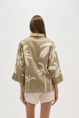 Camisa blanca con estampado de palmeras en color azul marino, de corte holgado, con cuello camisero, cierre frontal con botones y mangas 3/4 con puños anchos.