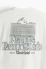Remera blanca de corte holgado con cuello redondo y estampado de Snoopy con la leyenda "Peanuts Racquet Club" en el pecho.