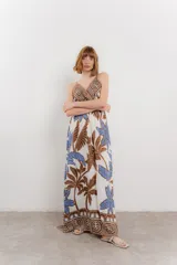 Vestido largo con estampado de hojas en tonos verdes y marrones sobre fondo blanco. Tiene breteles finos, escote en V y detalle de lazo en el frente. La falda es amplia y con vuelo.