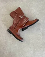 Bota de caña media de cuero negro con hebillas metálicas plateadas decorativas en la caña y alrededor del tobillo.