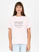Remera rosa con estampado frontal que incluye el número 1987, la frase 'Sports Club' y la palabra 'Manhattan'.