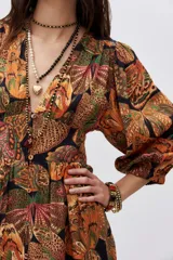 Vestido midi con estampado de mariposas en tonos naranja, verde y negro. Tiene escote en V, mangas largas abullonadas y abertura lateral en la falda.