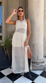 Vestido largo sin mangas, color blanco roto, confeccionado en tejido de red con trama abierta. Se lleva sobre una prenda interior blanca ajustada.