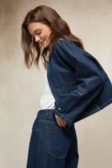 Sobrecamisa de denim azul oscuro, con cuello de pana color camel, cierre frontal de cremallera y dos bolsillos frontales con tapa y botón.