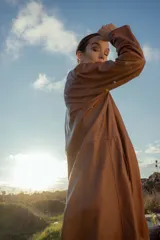 Gabardina marrón de cuero ovino italiano, con cuello camisero, cierre frontal con botones, mangas largas y corte recto.