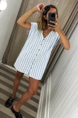 Vestido corto de tejido de punto, color celeste claro y blanco, con patrón de rayas verticales. Presenta escote en V y abotonadura frontal con botones metálicos.