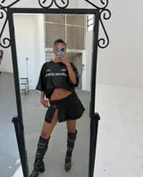 Minifalda negra de jean con tablas, abertura lateral y cinturón con hebilla metálica.