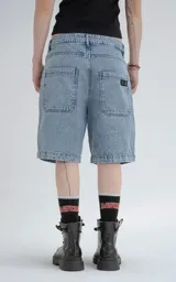 Bermuda de denim azul claro con efecto desgaste, corte oversize y estilo carpintero con bolsillo lateral.