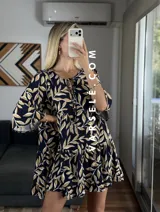 Vestido corto color verde oliva con estampado de hojas en blanco y negro, escote con lazo ajustable y mangas 3/4 acampanadas.