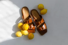 Sandalias de cuero color marrón con dos tiras anchas cruzadas en el empeine y suela plana.