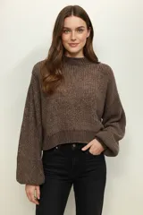 Sweater de tejido grueso, color marrón jaspeado, con cuello redondo alto y mangas largas abullonadas. El calce es holgado y corto (cropped).