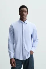 Camisa celeste a rayas verticales blancas, de corte recto, con cuello italiano abierto, mangas largas con puños abotonados y cierre frontal con botones.