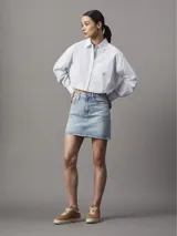 Camisa cropped de popelina de algodón suave a rayas verticales celestes y blancas, de corte relaxed, con cuello en punta, puños segados, bajo redondeado y bolsillo en el pecho con insignia con el logo de Calvin Klein.