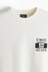 Remera color crema de algodón con cuello redondo y mangas cortas. Estampado frontal con imagen de radiograbador y texto "It might get loud". Corte holgado.