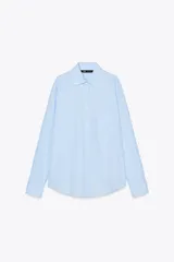 Camisa celeste con rayas verticales blancas, de corte amplio, cuello clásico, manga larga con puños abotonados, bolsillo de plastrón en el pecho y cierre frontal con botones.