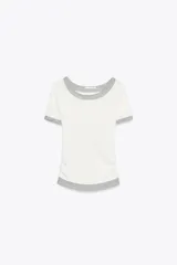 Camiseta blanca de corte slim fit, cuello redondo y manga corta con acabados en puntilla. Tiene detalle de frunces en los laterales y tejido combinado a contraste efecto doble en cuello, mangas y ruedo.