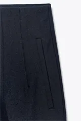 Pantalón negro de vestir, de tiro alto, corte recto y largo al tobillo. Presenta bolsillos laterales y cierre frontal con cremallera, botón interior y gancho metálico.