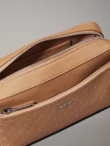 Bandolera Calvin Klein color marrón claro con estampado del logo de la marca. Tiene correa ancha ajustable, cierre de cremallera, bolsillo exterior delantero y bolsillo interior.