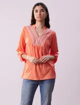 Blusa blanca de poliéster y rayón con escote en V bordado y mangas tres cuartos regulables con presilla y botón.