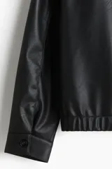 Campera negra de cuero sintético con cuello clásico, cierre frontal con cremallera, dos bolsillos delanteros con solapa y puños y bajo elásticos.