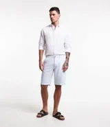 Bermuda de hombre en lino color celeste, de corte recto, sin estampado y con textura discreta. Presenta trabillas en la cintura, cierre frontal con botón y cremallera, y bolsillos laterales.