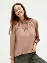 Blusa blanca de mangas largas con cuello fruncido y lazo.