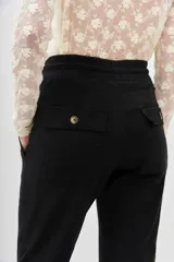 Pantalón tipo babucha negro, confeccionado en gabardina elastizada, con cintura regulable mediante cordón y puños ajustados en flame. Posee bolsillos diagonales delanteros y bolsillos con solapa y botón traseros.