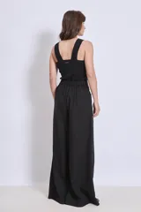 Pantalón negro de corte palazzo con apliques bordados en color crema en la parte inferior de una pierna.