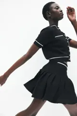 Minifalda negra tableada de punto con cintura elástica a rayas horizontales blancas y negras.