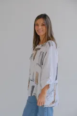 Blusa blanca de lino con estampado abstracto en tonos marrones y grises, de corte holgado y mangas 3/4 con puños abotonados.