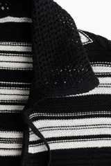 Buzo corto de punto con rayas horizontales blancas y negras, cuello polo, mangas largas y cordones negros.
