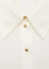 Camisa blanca de poliéster con cuello camisero, cierre frontal con botones y mangas largas con puños abotonados. Diseño recto y tejido fluido.