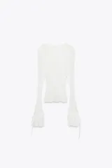 Top semitransparente de encaje blanco, con cuello redondo y mangas largas acampanadas con volantes ajustables con lazada.