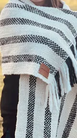 Chal bufandón tejido a telar con lana virgen sin teñir y lana negra teñida a mano, con diseño de rayas blancas y negras y flecos en los extremos.