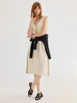 Vestido color crudo, de corte recto y largo a la rodilla, sin mangas y con escote en V. Presenta detalle de costura en zigzag a lo largo de los laterales.