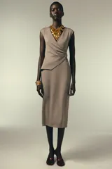 Vestido midi color beige, de corte recto, con escote en pico cruzado, sin mangas y detalle de hebilla metálica en la cintura.