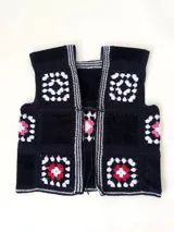 Chaleco sin mangas, confeccionado con cuadrados de cuero negro perforado combinados con cuadrados de crochet en hilo de algodón negro y blanco, con detalles centrales en rojo.