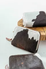 Billetera de cuero con estampado animal print de vaca en blanco y negro, con cierre de cremallera.