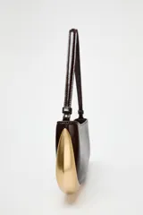 Bolso de hombro alargado color marrón oscuro con detalle metálico dorado en un lateral, asa corta y cierre de cremallera.