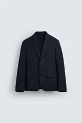 Blazer azul marino de corte regular fit, confeccionada en tejido de algodón con elasticidad. Sin forro interior, con cuello de solapas de muesca, manga larga con puños abotonados, bolsillos de solapa en la cadera, bolsillo interior, aberturas en la espalda y cierre frontal con botones.