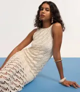 Vestido midi de crochet color crudo, sin mangas y con cuello redondo. Presenta aberturas laterales en el ruedo.