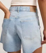 Bermuda de denim para mujer con cintura media y bajo deshilachado. Cuenta con trabillas en la cintura, cierre tradicional y bolsillos funcionales. Confeccionada en algodón con un toque de elastano.