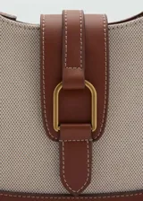 Bolso tipo hobo de lona color beige con detalles en cuero marrón. Tiene asa corta ajustable, cierre con solapa y botón magnético, bolsillo interior y forro de algodón.