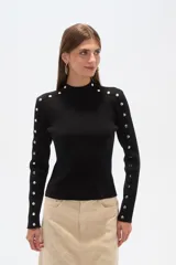 Sweater negro de punto con cuello alto y botones metálicos decorativos en hombros y mangas largas.