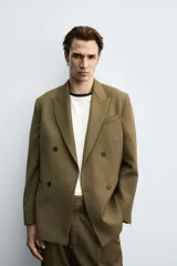 Blazer color verde oliva de corte regular, confeccionada en tejido con lana. Presenta cuello con solapas de pico, manga larga con puños abotonados, bolsillo de vivo en pecho, bolsillos de doble vivo en cadera, bolsillo interior y aberturas en la espalda. Cierre frontal cruzado con doble botonadura.