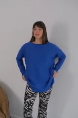 Buzo azul de viscosa con cuello redondo y manga larga. Presenta un aplique con diseño geométrico en el brazo izquierdo.
