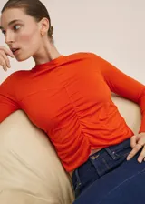 Remera naranja de manga larga con detalle fruncido en el centro y escote redondo.