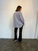 Camisa a rayas verticales azules y blancas, de popelina de algodón, con cuello verde y botones marmolados. Es corta adelante y larga atrás.