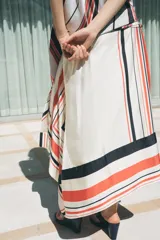 Falda midi de tiro medio con estampado de rayas rojas, negras y blancas. Tiene bajo asimétrico y cierre frontal tipo pareo ajustable con lazos negros.