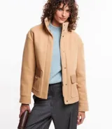 Saco color beige en polyvelour, con cuello alto, mangas largas, sisas desplazadas, cierre delantero y bolsillos con detalle en PU.